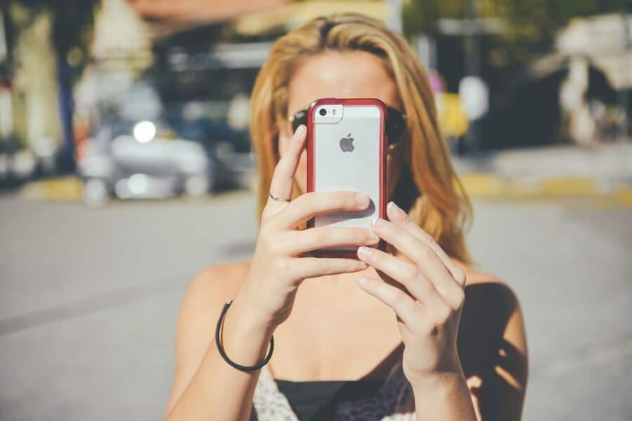 blonde woman taking a selfie in the street with an iphone