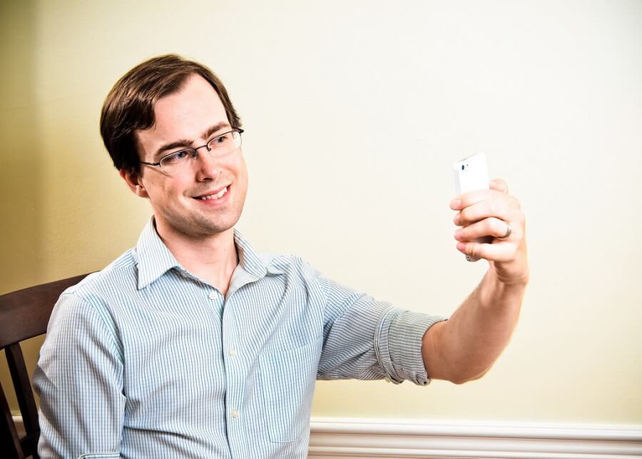 man with glasses smiling while taking a selfie