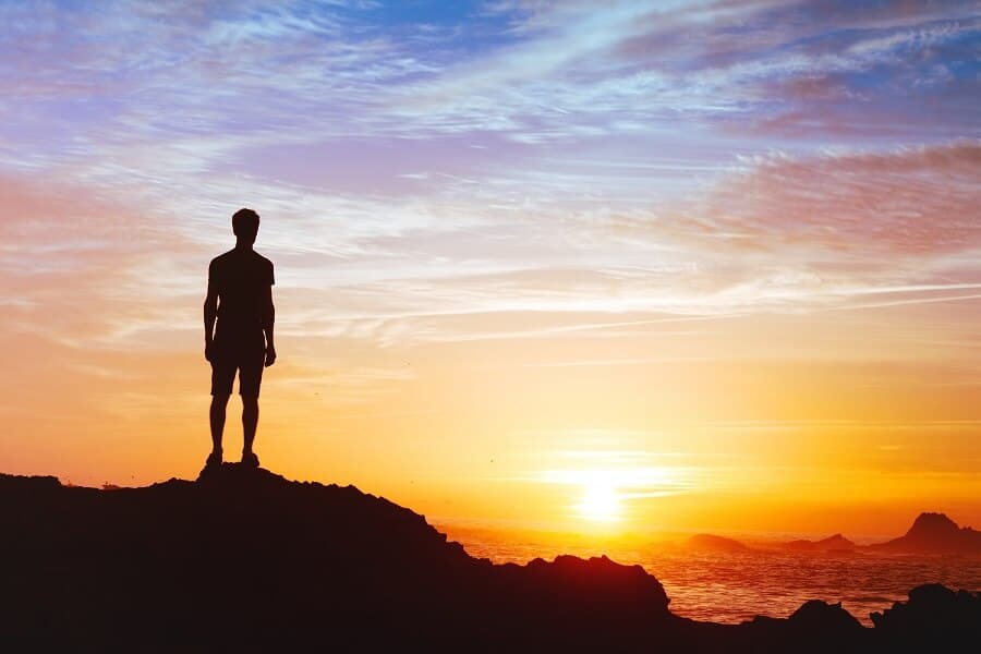 man standing on a cliff and admiring the sunset