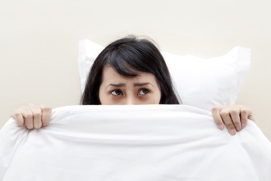 woman covering her face with a sheet in bed