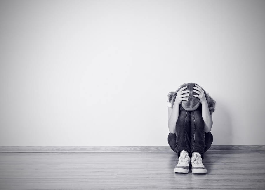 young girl covering her head and sitting with her back against a wall