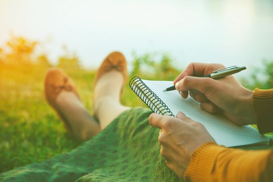 girl laying in the grass and writing something in a notebook
