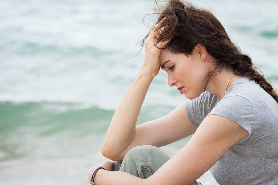 young woman looking down with sadness while sitting on the beach