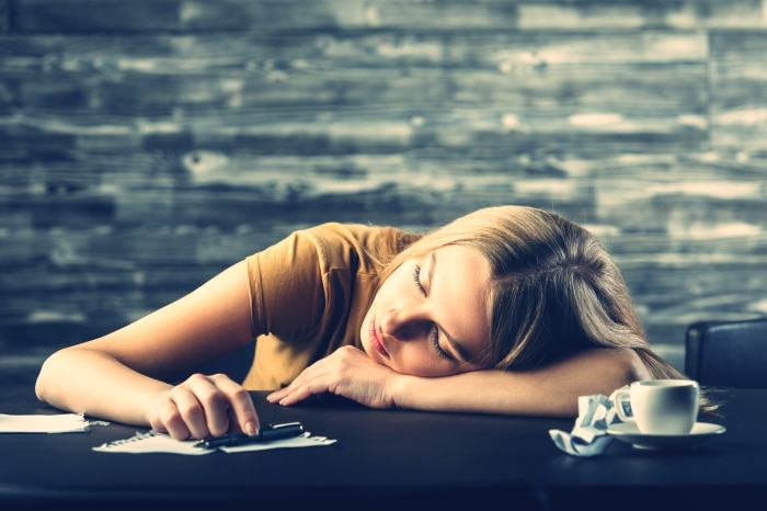 Tired young woman sleeping on wooden office desk
