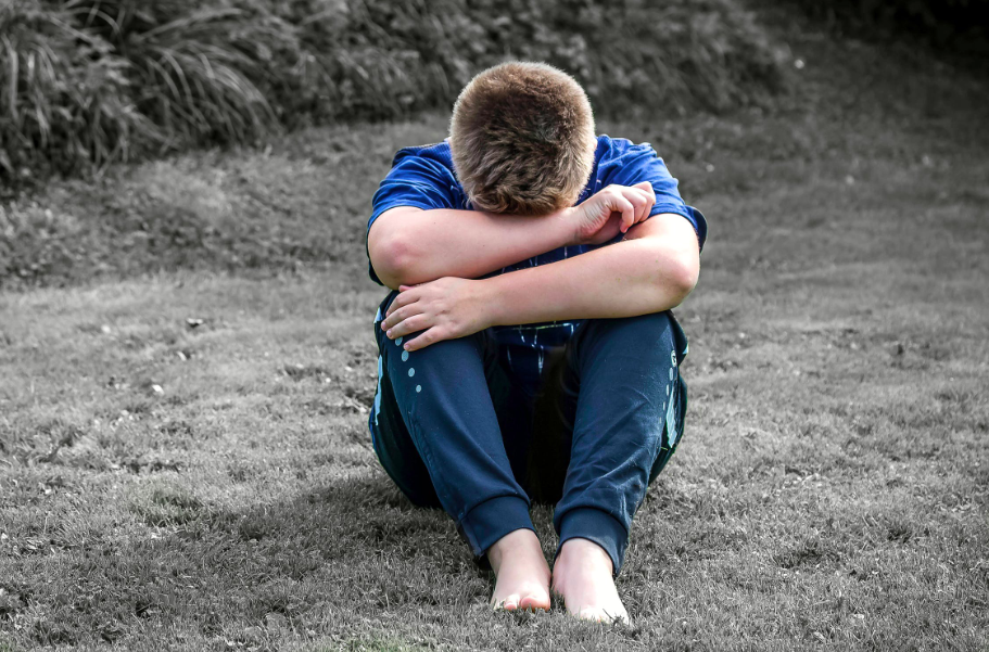 inferiority complex: rear view of a boy sitting on grassland